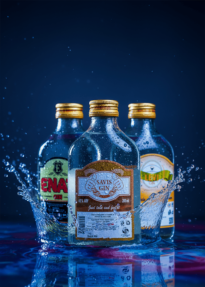 Three gin bottles splashing creatively under vibrant studio light.